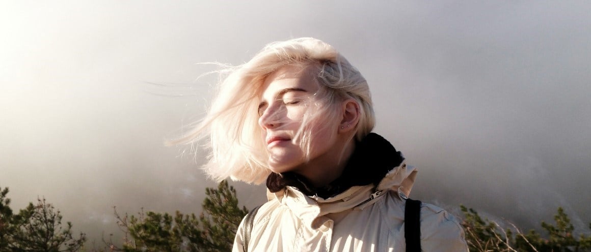 Young woman in nature with a relaxed expression, closed eyes with the sun on her face.